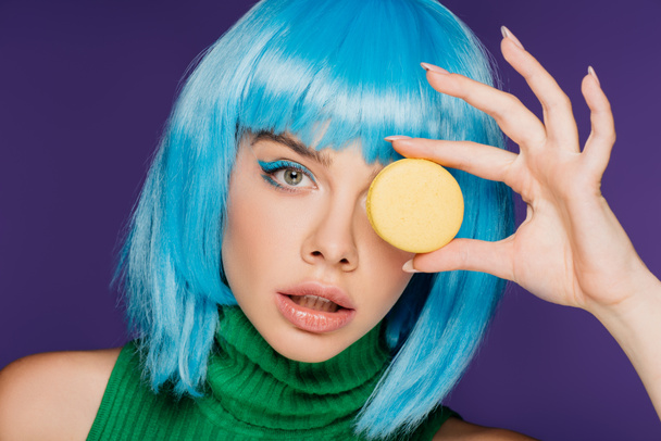 schönes Mädchen in blauer Perücke posiert mit süßem Macaron isoliert auf lila - Foto, Bild