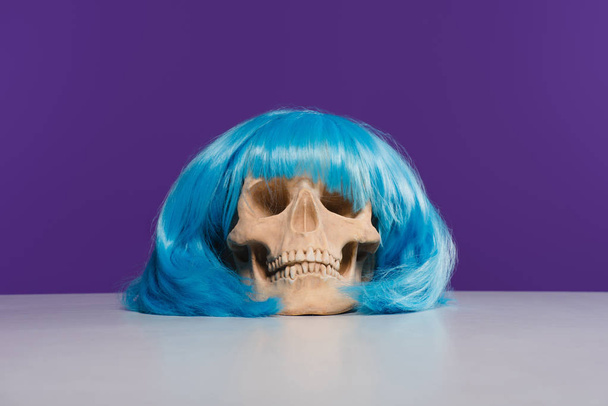 Czaszka w niebieski wig na stole z fioletowym tle - Zdjęcie, obraz