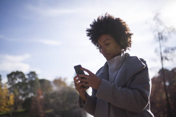 belle afro femme avoir du plaisir dans le parc avec son téléphone intelligent
  - Photo, image