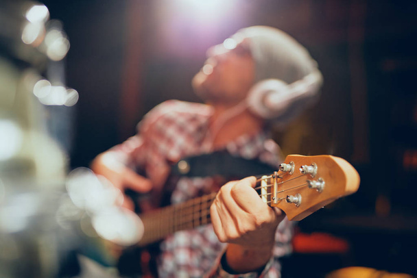 Gros plan du jeune musicien jouant de la guitare basse avec des écouteurs sur les oreilles
. - Photo, image