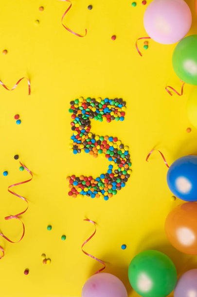 Ευτυχισμένος γενέθλια αριθμό 5 κατασκευασμένα από καραμέλες με πολύχρωμα μπαλόνια σε κίτρινο φόντο. - Φωτογραφία, εικόνα