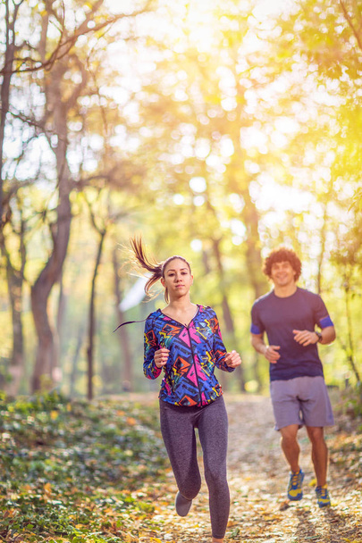 νεαρό ζευγάρι απολαμβάνει σε έναν υγιεινό τρόπο ζωής ενώ τζόκινγκ κατά μήκος μια έννοια δάσους, άσκηση και το γυμναστήριο - Φωτογραφία, εικόνα