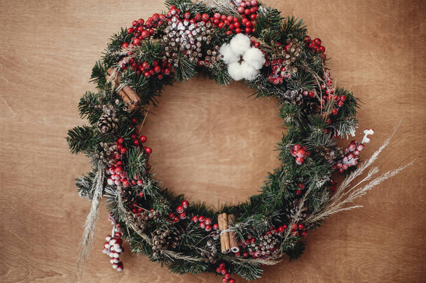 クリスマスの花輪, フラット横たわっていた。赤い果実、松ぼっくり、シナモン、モミの枝は、素朴な木製の背景、トップ ビューでコットンします。大気の不機嫌そうなイメージ。メリークリスマス - 写真・画像