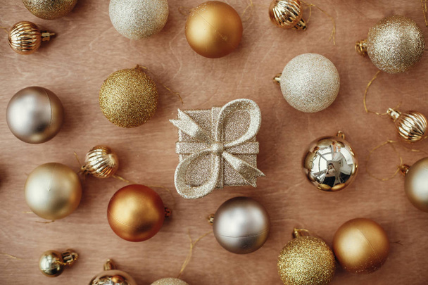 Merry Christmas. Christmas golden glitter gift box and shiny baubles and balls on rustic background, flat lay. Modern gold decorations and present. Seasons greetings. Happy holidays - 写真・画像