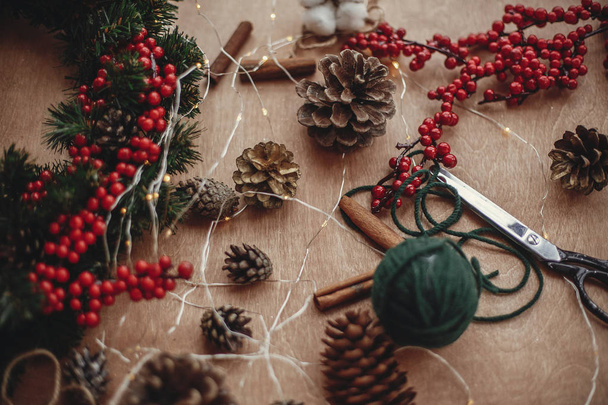 Rustikální vánoční věnec. Větve jedle, věnec, červené bobule, šišky, nit, nůžky, skořice, bavlny na rustikální dřevěné pozadí. Vánoční věnec na výrobu - Fotografie, Obrázek