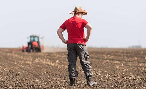 Un agriculteur examine un champ de blé planté pendant que le tracteur laboure
 - Photo, image