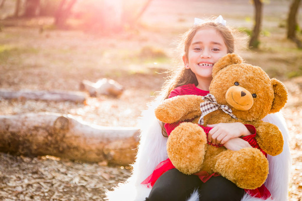 Νέοι χαριτωμένο μικτή φυλή κορίτσι αγκαλιάζει αρκουδάκι σε εξωτερικούς χώρους. - Φωτογραφία, εικόνα