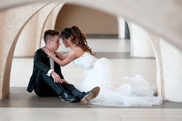 newlyweds are sitting on the floor in the arch on their wedding day in a wedding dress - Foto, Imagem