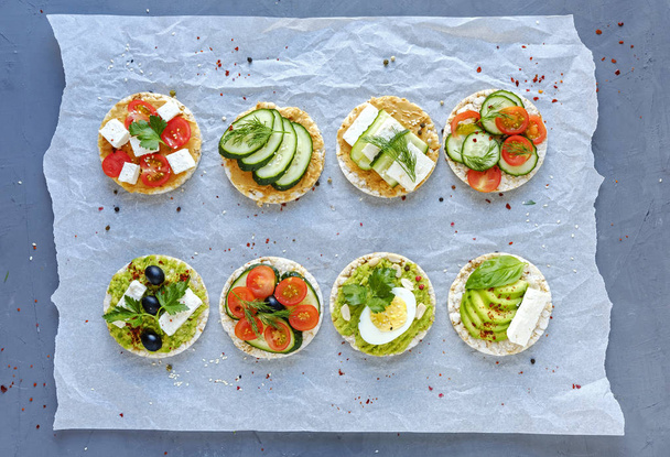 Разнообразные вкусные закуски со свежими овощами, сыром фета и яйцом на мятой бумаге, смотрящейся сверху двумя аккуратными рядами
 - Фото, изображение