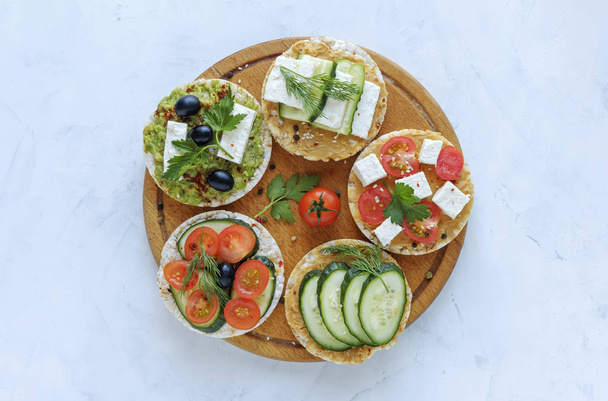 Homemade delicious appetizers on rice cakes with fresh veggies, feta cheese, herbs and boiled egg served on a wooden board over blue - Photo, Image