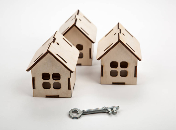 Три деревянных миниатюрных домика и ключ от двери на белом фоне
 - Фото, изображение