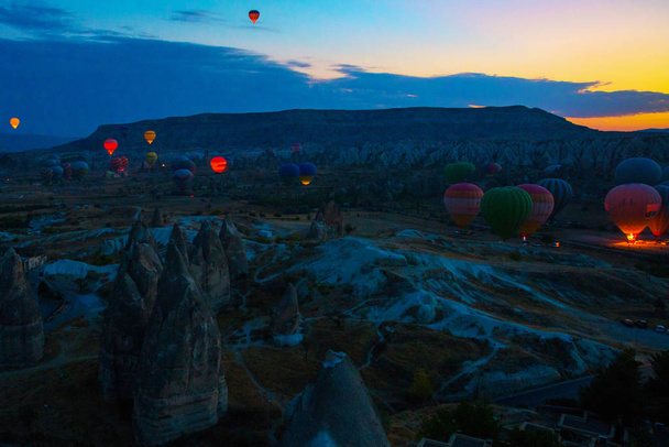 Cappadocia, Goreme, Anatolia, Turkey. Hot air balloons floating in the sky with backlit colorful background behind. Favorite entertainment for tourists. - Foto, afbeelding