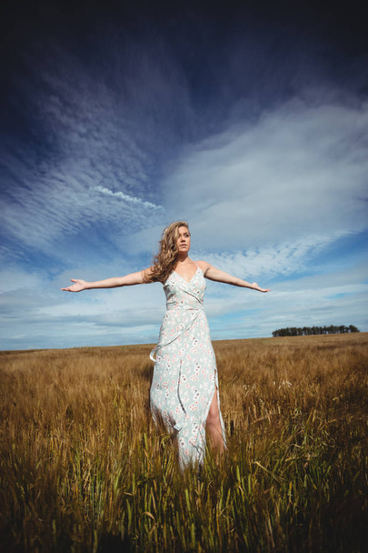Donna in piedi con le braccia tese nel campo di grano nella giornata di sole
 - Foto, immagini
