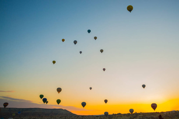Cappadocia, Goreme, Anatolia, Turkey: Scenic vibrant view of balloons flight in Cappadocia valley in sunrise rays. Popular and favorite entertainment for tourists. - Фото, изображение