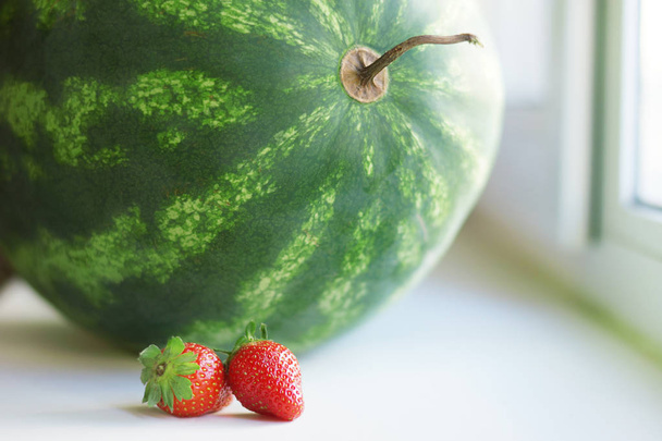 スイカとイチゴの大きさの異なる二つの果実。健康的な食事とダイエットのための概念として赤と緑の甘いの新鮮な果物   - 写真・画像