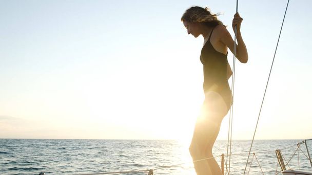 Nuori hoikka tyttö valmistautuu hyppäämään purjehdusjahdilta avomerelle auringonlaskussa.
 - Valokuva, kuva