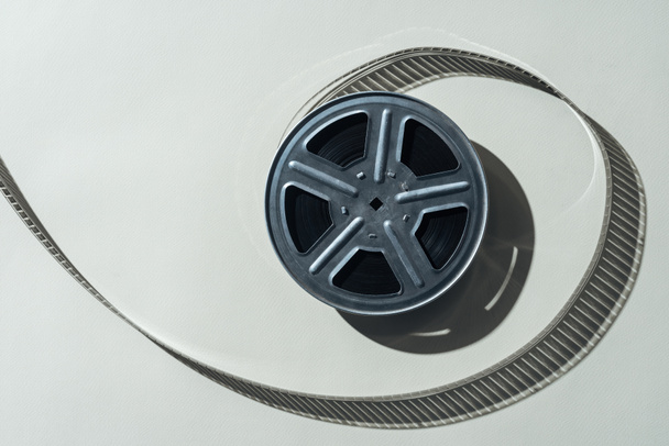 top view of film reel with twisted cinema tape on grey background - Foto, afbeelding