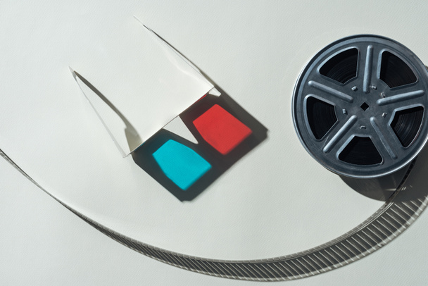 top view of 3d glasses with shadow and film reel with twisted cinema tape on grey background - Photo, Image