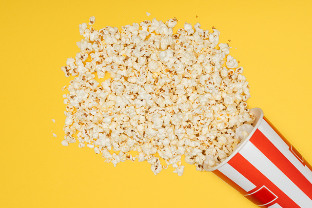 top view of overturned striped bucket with popcorn isolated on yellow - Foto, Imagen