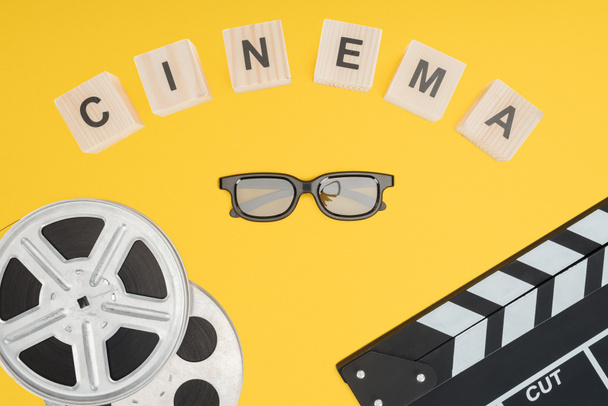 cubos de madeira com letras "cinema", clapperboard, bobinas de filme e óculos 3d estereoscópicos isolados em amarelo
 - Foto, Imagem