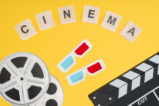 cubes with "cinema" lettering, 3d glasses, clapperboard and film reels isolated on yellow - Foto, afbeelding