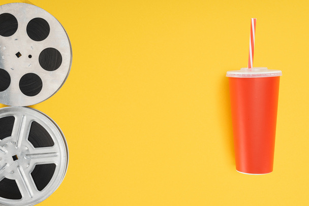 film reels and red disposable cup with straw isolated on yellow  - Фото, изображение