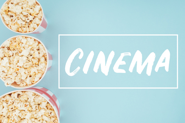 top view of buckets with popcorn in vertical row and "cinema" lettering isolated on blue - Фото, зображення