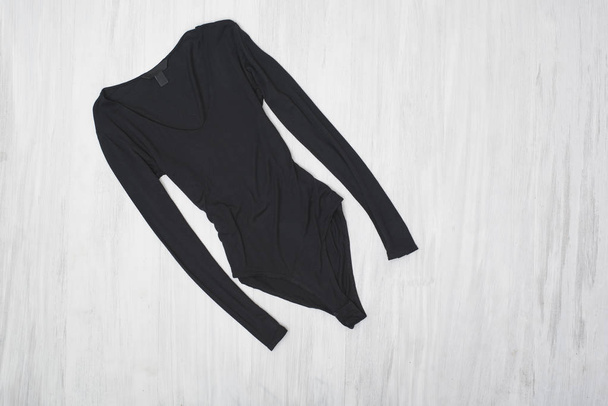 Black bodysuits with sleeves on a wooden background. Fashionable concept - Φωτογραφία, εικόνα