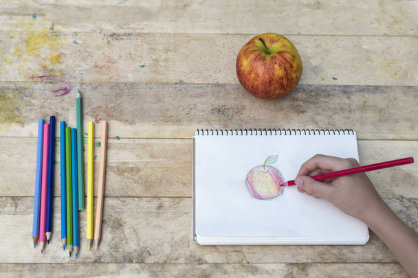 Τα χέρια των παιδιών να σχεδιάσετε ένα μήλο με χρωματιστά μολύβια. Το Top view - Φωτογραφία, εικόνα