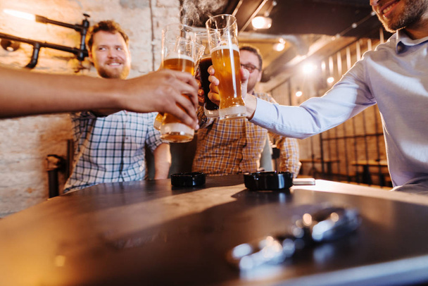 young happy bearded men celebrating and toasting with beer in pub - Photo, Image