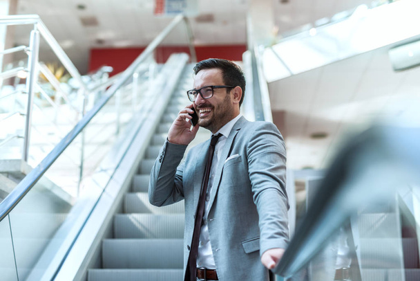 Close up of happy businessman standing on stairs and using smart phone. Suit and eyeglasses on. - Foto, Imagen