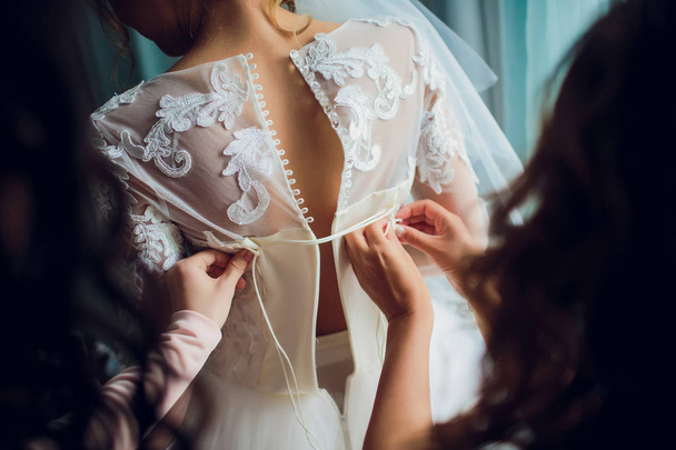 Bridesmaid makes bow-knot on the back of brides wedding dress - Photo, image