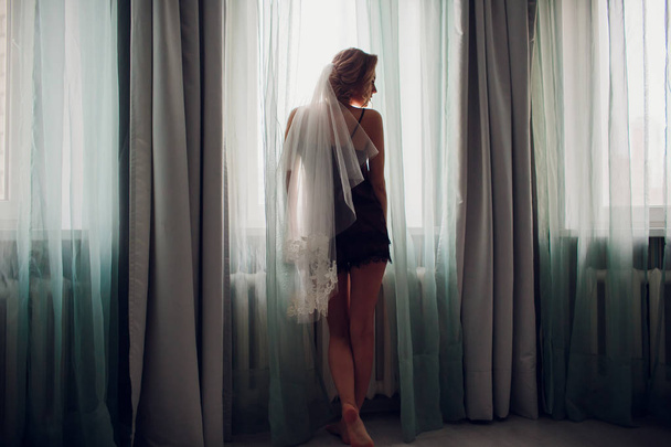 girl in a wedding veil near a window in a dark room - Foto, Imagen