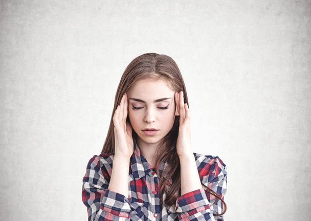 Portrait of beautiful young woman with long fair hair wearing checkered shirt having a headache. Concrete wall background. Concept of stress and overworking - Photo, image