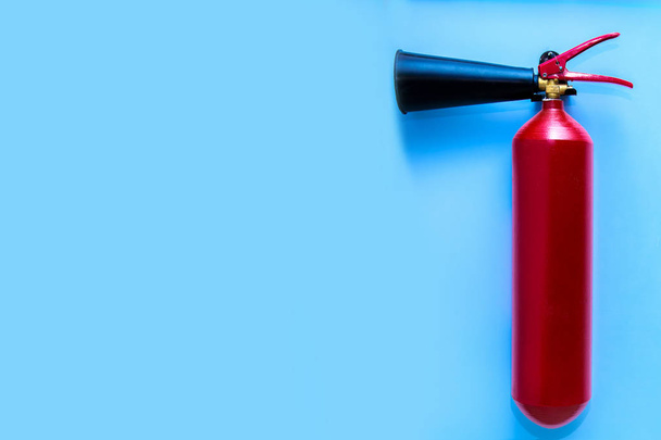 An iron extinguisher of red color is installed against the background of a blue wall with a free space for text. - Photo, image