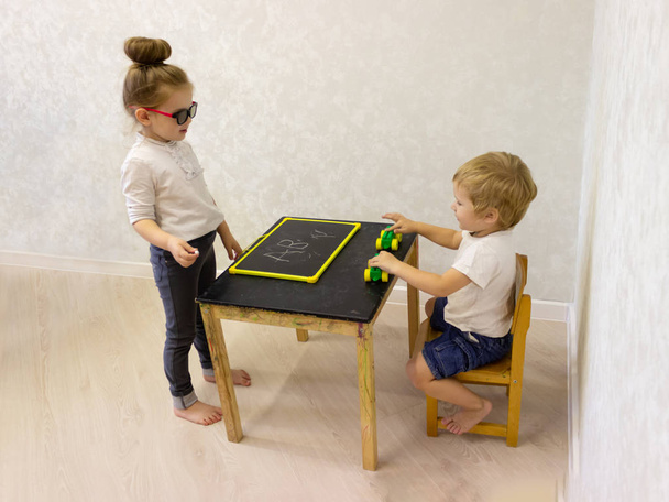 Sister and brother are playing school. The boy of preschool age is not ready to learn, he wants to play with typewriters. The teacher and the student are engaged. Pros and cons of early development. - Foto, Imagen