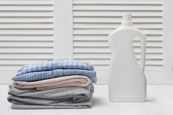 Пачка сложенной одежды и бутылка моющего средства. Белый фон
 - Фото, изображение