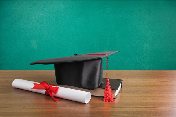 Graduation hat, book and diploma on wooden table - Fotoğraf, Görsel