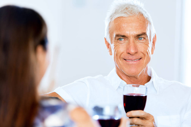 Senior man with holding a glass of wine indoors - Fotó, kép