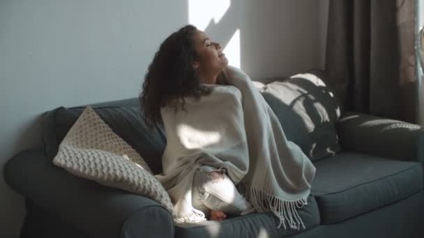 Happy beautiful woman sitting on sofa wrapped in blanket relaxing at home. - Imágenes, Vídeo