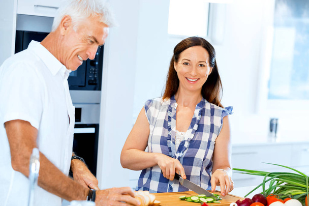 Happy mature couple cooking together at home - Foto, afbeelding