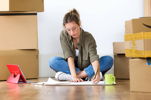 Foto de una mujer joven y bonita dibujando planos de su nueva casa mientras estaba sentada en el suelo en casa
. - Foto, Imagen