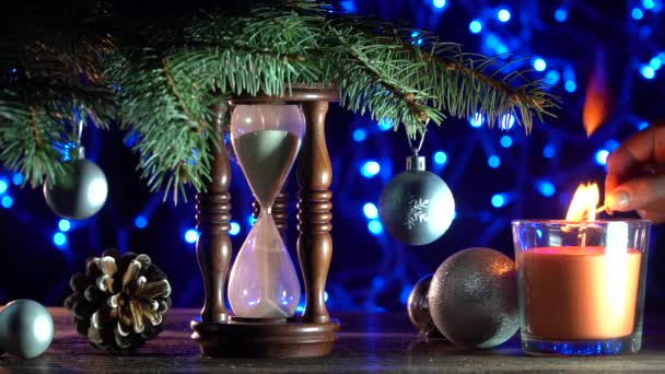 Xmas decoratie. Kerstmis achtergrond, een zand klok onder een boom van spar, waarmee wordt aangegeven hoe lang het tot het nieuwe jaar. Bovenaanzicht. Een dame licht een kaars. Gefilmd in 4 k-resolutie - Video