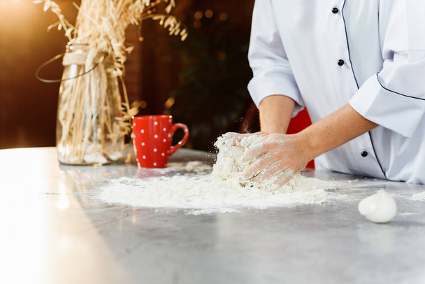Mains de boulanger pétrissant la pâte sur la table avec de la farine, des œufs et d'autres ingrédients
. - Photo, image