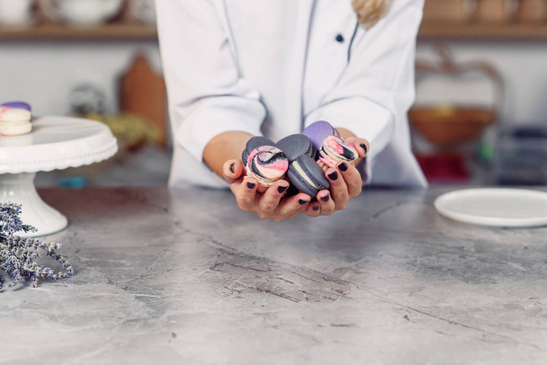 Female hands holding colorful french macaroons over a marble table. - 写真・画像