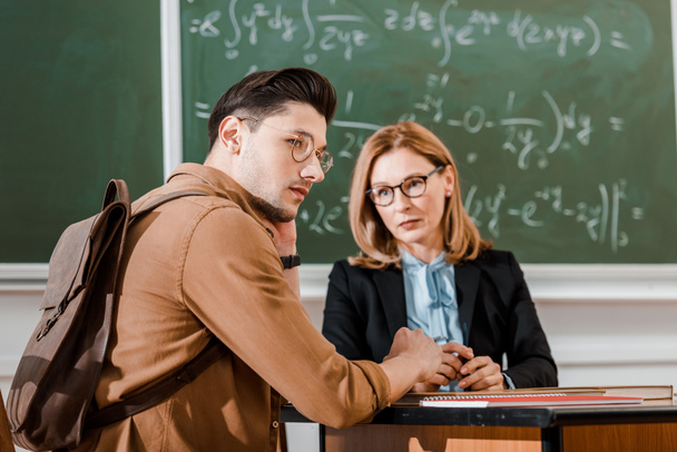 Profesora mirando a una joven estudiante en el aula con pizarra en el fondo
  - Foto, Imagen