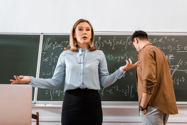 Жіночий вчитель жестикулює в класі в формальному одязі біля студента
 - Фото, зображення