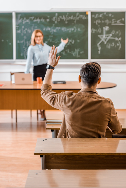 Selective focus of male student raising hand in classroom  - Foto, afbeelding