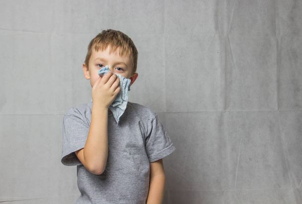 Un garçon en T-shirt gris tenant un mouchoir près de son nez
 - Photo, image