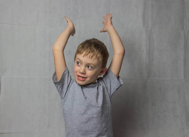 El niño en una camiseta gris en una fuerte delicia levantó las manos y se regocija
 - Foto, imagen